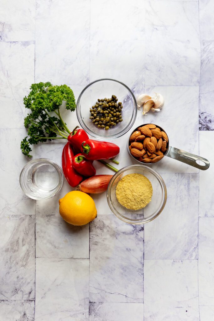 display of ingredients: red peppers, almonds, capers, lemon, shallot, nutritional yeast and parsley