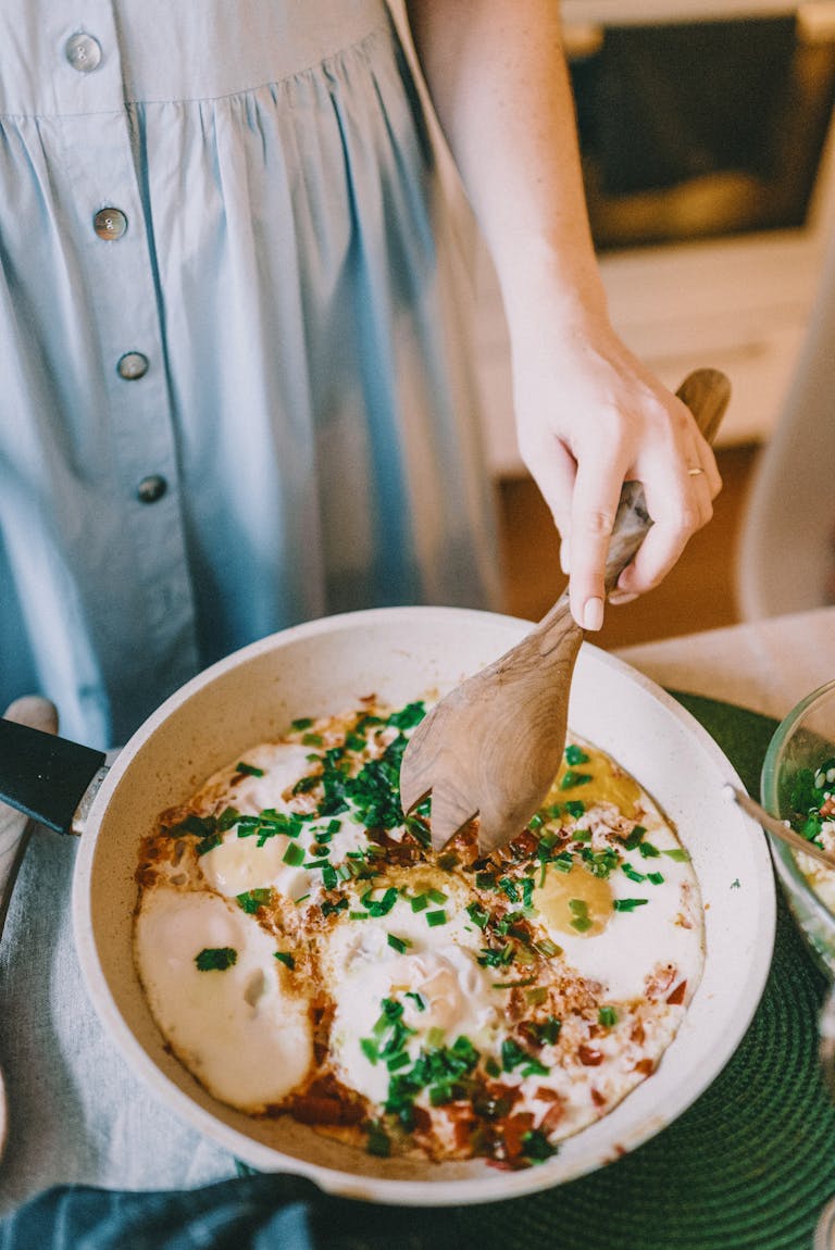 A chef preparing Shakshuka with eggs, tomatoes, and herbs in a skillet.